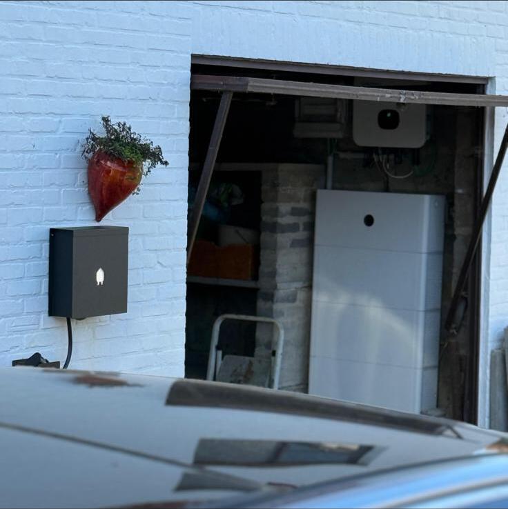 Zwarte laadpaal aan witte gevel naast de garage